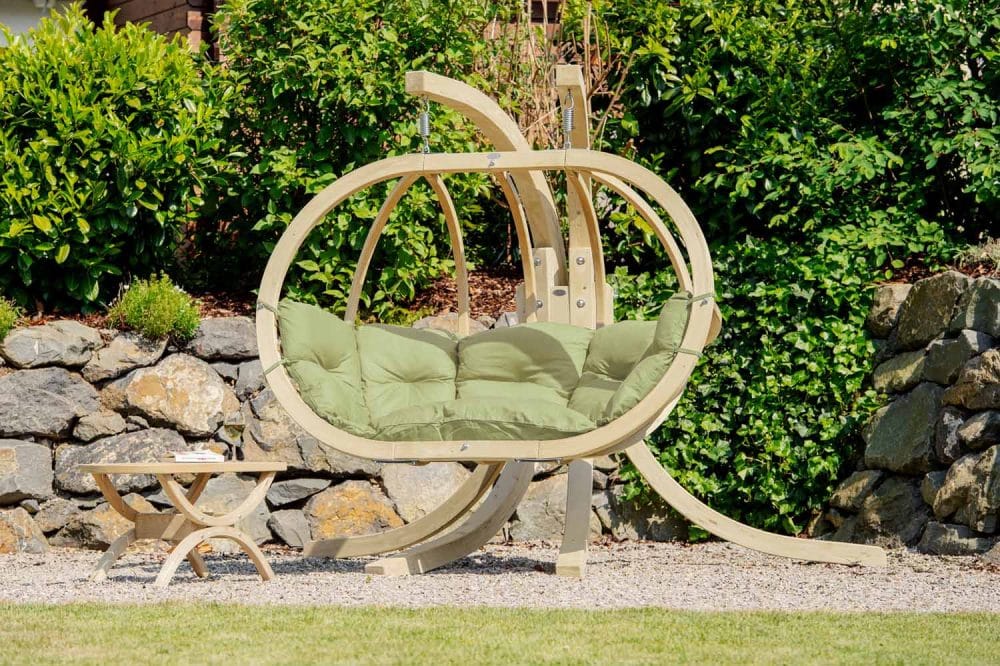 Oval bred hängstol i trä med tjocka dynor i ljust olivgrön utomhus